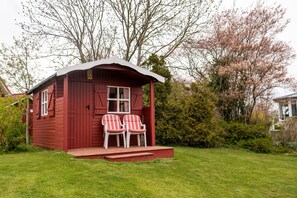 A small red wooden cabin with a porch and two striped chairs.
