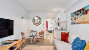A modern living room with a flat-screen TV, wooden dining table, and chairs. There is a sofa with cushions and a painting on the wall. - 3 Bedroom Home in City Central + FREE PARKING (Auckland CBD)