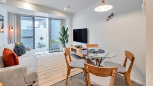 A modern living room with a glass dining table, wooden chairs, a sofa, and a TV. - 3 Bedroom Home in City Central + FREE PARKING (Auckland CBD)