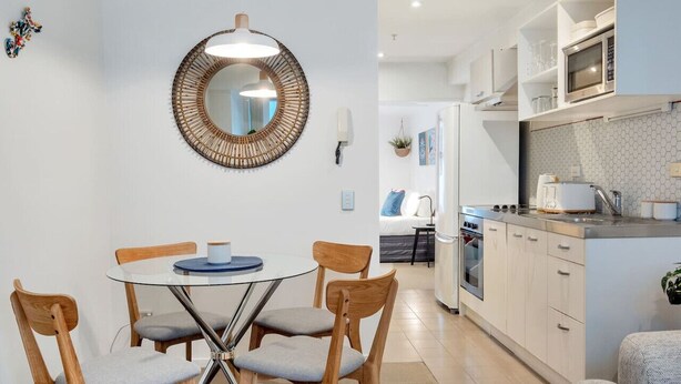 A modern kitchen with white cabinets, a microwave, and a toaster. There is a dining area with a round table and wooden chairs. - 3 Bedroom Home in City Central + FREE PARKING (Auckland CBD)