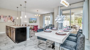 Una cocina moderna con una isla central, un comedor con una mesa larga y un amplio ventanal corredizo al exterior.