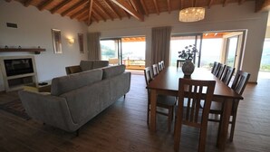 Un salon spacieux avec un plafond en bois, un canapé gris, une table à manger avec des chaises et une cheminée.