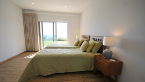 Une chambre avec deux lits, un plancher en bois, une table de chevet avec une lampe et une vue sur l’extérieur, accessible par une porte-fenêtre coulissante.