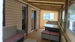 Une terrasse couverte avec une plateforme en bois, une table avec des bancs et des portes-fenêtres coulissantes donnant sur un espace extérieur.