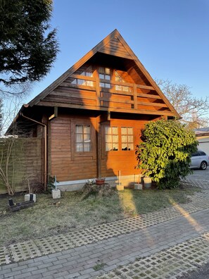 A wooden house with a sloped roof, a small porch, and a brick pathway leading to the entrance.