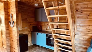 Uma cozinha compacta com paredes de madeira, bancada azul e escada de madeira.