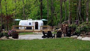 Une maison mobile dotée d’un porche abrité, d’un espace salon extérieur et entourée d’une zone boisée.