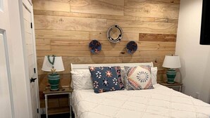 Une chambre à coucher avec une tête de lit en bois, un couvre-lit blanc, des coussins à motifs et deux tables de chevet avec des lampes.