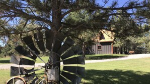 Un molino rústico con una bicicleta, frente a una casa y árboles.