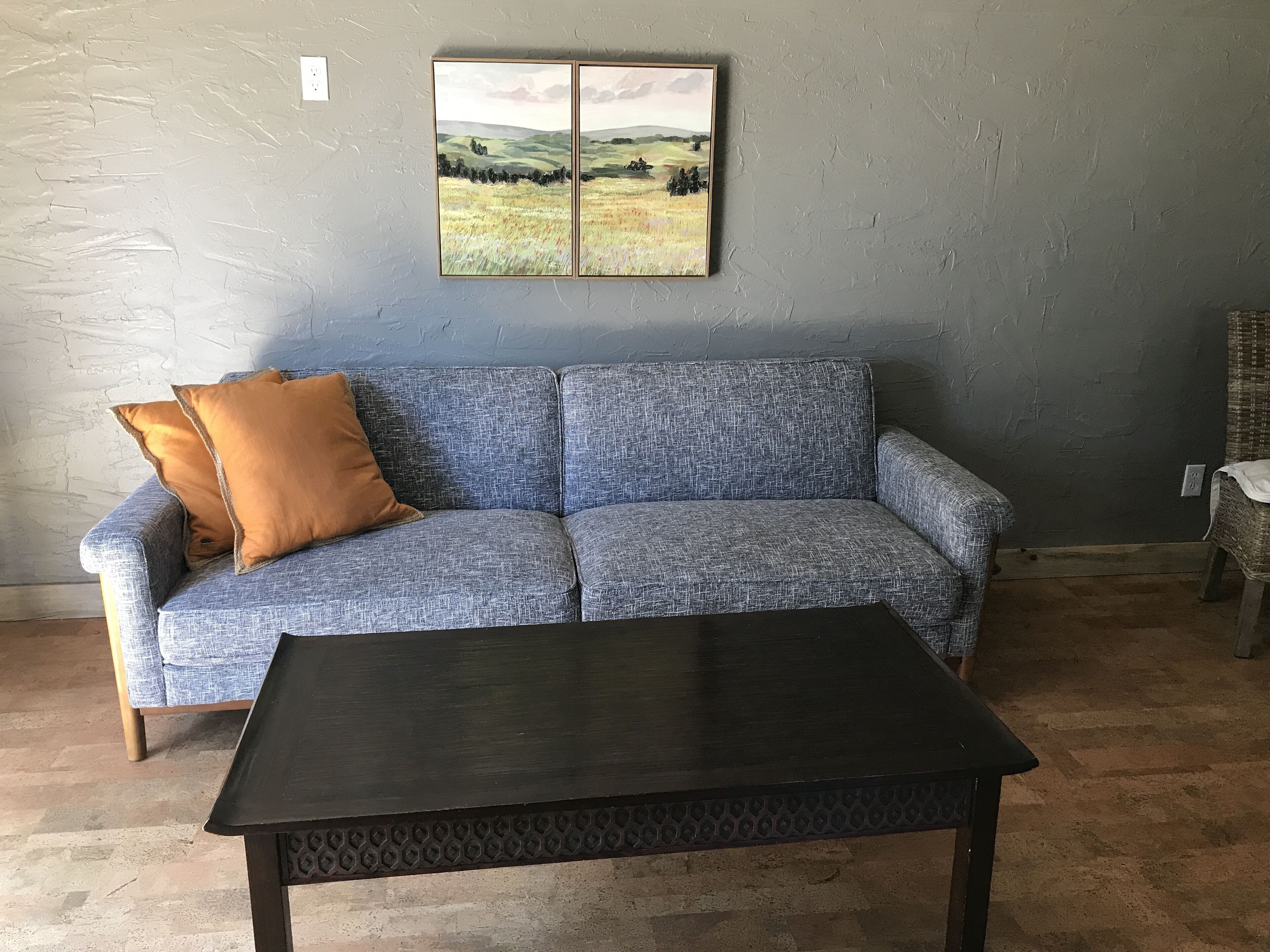 A room with a blue textured sofa, a dark wooden coffee table, and a landscape painting on the wall.