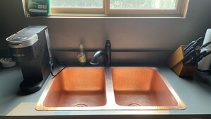 Una cocina con un lavamanos doble, una cafetera y una botella de detergente.