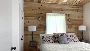 Ein Schlafzimmer mit Holzboden, einem Bett mit weißer Bettdecke, zwei Nachttischlampen und einem Fenster mit Vorhängen.