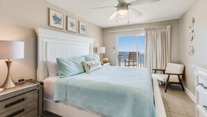 Une chambre à coucher avec un lit, des tables de chevet, un ventilateur de plafond et une vue sur l’océan.