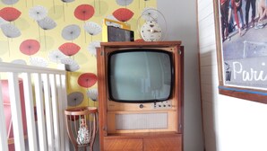 Ein alter Fernseher steht auf einer Holzkabine vor einer Wand mit Muster.