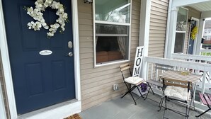 Eine einladende Veranda mit einer dunkelblauen Tür, einem Kranz, einem Schild mit der Aufschrift 'NO SOLICITING', einer Bank und einem Schild mit dem Wort 'HOME'.