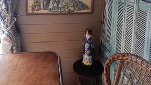 A room with three framed paintings on the wall, a small table with a decorative figure, and a wicker chair. - Appartement "voyage Autour du Monde" (Bordeaux)