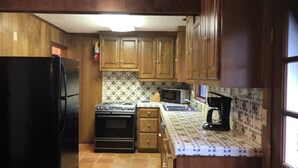 Una cocina con armarios de madera, un refrigerador negro, un horno, un microondas y una cafetera.