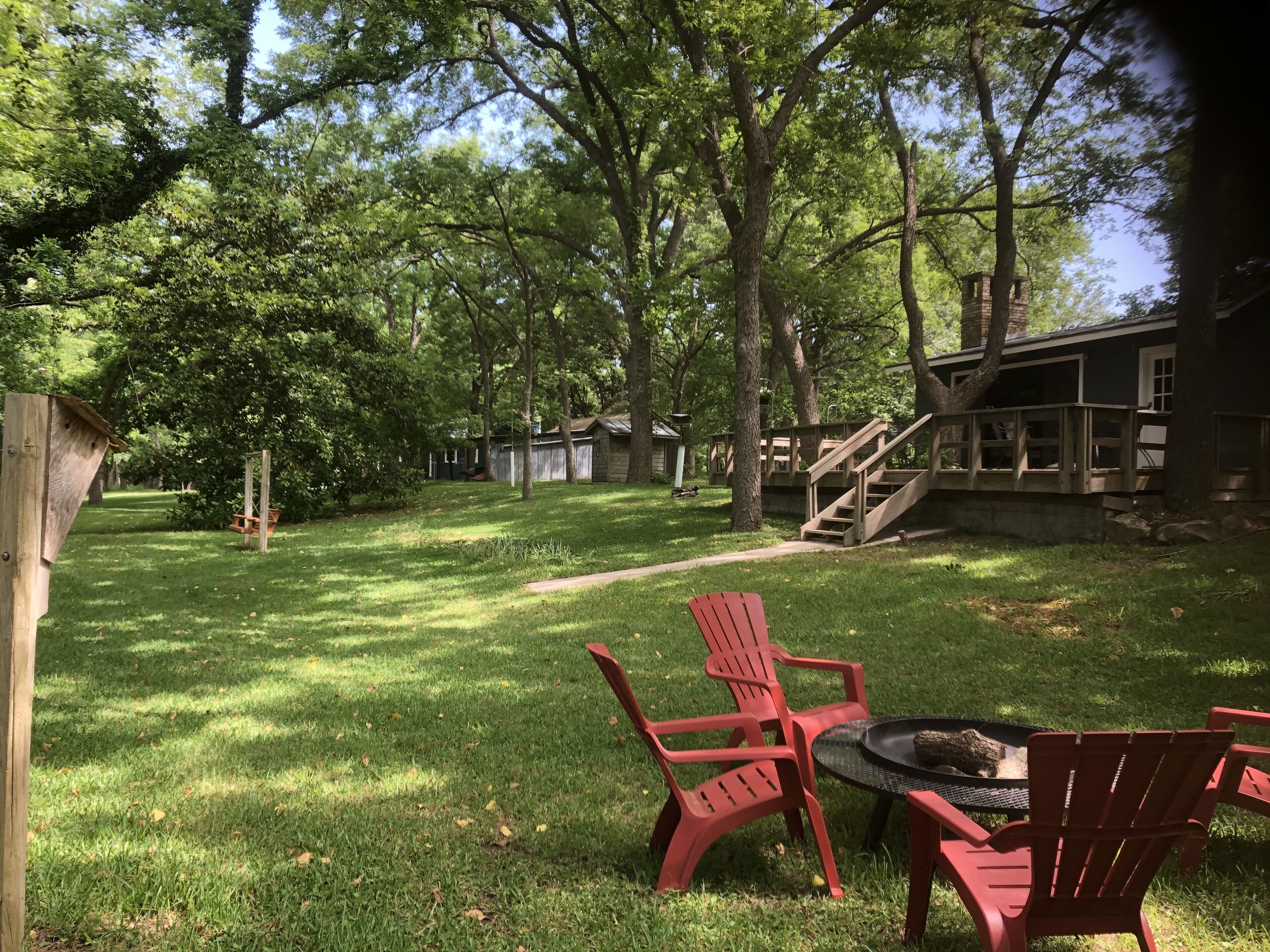 A backyard with a wooden deck, a fire pit, and red Adirondack chairs.