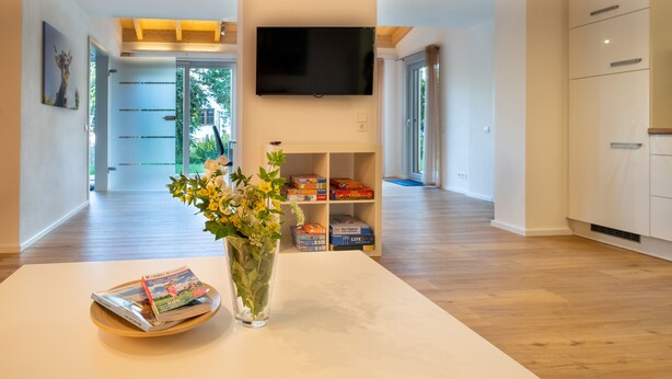 Una sala de estar moderna con un televisor de pantalla plana, una estantería y un florero con flores sobre una mesa.