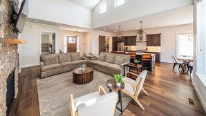 A spacious living area with a large sectional sofa, a coffee table, and a dining area with a kitchen in the background. - Juniper Ranch - Golf Cart Included | Sleeps 10 (Powell Butte)
