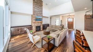 A spacious living area with a stone fireplace, a large sofa, and a dining table with benches. - Juniper Ranch - Golf Cart Included | Sleeps 10 (Powell Butte)