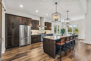A modern kitchen with dark wood cabinets, stainless steel appliances, and a central island with bar stools. - Juniper Ranch - Golf Cart Included | Sleeps 10 (Powell Butte)