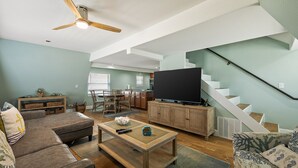 A spacious living room with a high ceiling fan, a large flat-screen TV, a wooden coffee table, and a comfortable seating area.