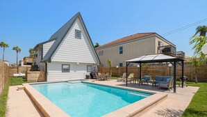 A backyard with a swimming pool, a covered patio, and a house with a sloped roof.