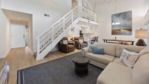 Un vaste espace de vie doté d’un haut plafond, d’un escalier menant à un niveau supérieur, d’une grande fenêtre et offrant une vue sur l’extérieur.