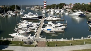 Un port de plaisance où sont amarrés de nombreux bateaux, un phare en arrière-plan et un ciel dégagé.