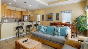 A spacious living area with a gray sofa, wooden chairs, a dining table, and a ceiling fan.