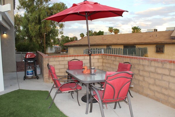 Une terrasse extérieure avec une table et des chaises, un parasol rouge et un barbecue.