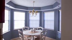 A dining area with a round table, white chairs, and a chandelier. - Convenient Creekside condo with large wrap around balcony, close to everything! (Gatlinburg)