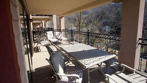 A balcony with a table and chairs, a railing, and a view of trees and mountains. - Convenient Creekside condo with large wrap around balcony, close to everything! (Gatlinburg)