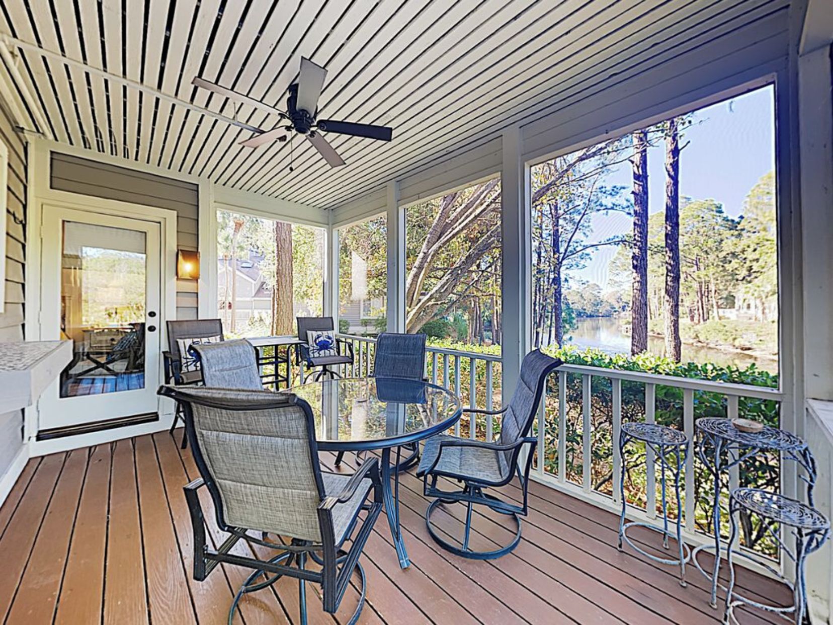 A covered outdoor patio with a table and chairs, a ceiling fan, and a view of a lake and trees.