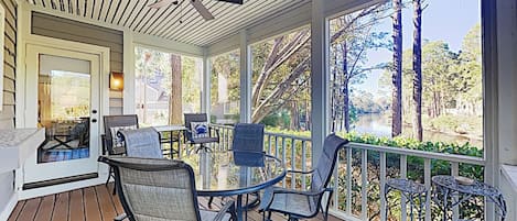 A covered outdoor patio with a table and chairs, a ceiling fan, and a view of a lake and trees.
