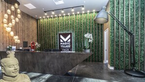 Uma área de recepção com design moderno, destacando um balcão de madeira, um painel vertical com jardim verde e um grande letreiro iluminado com a inscrição "MAGIC VILLAGE Views".