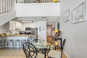 Enjoy meals at the glass-top dining table surrounded by artwork and a staircase leading to an upper level.