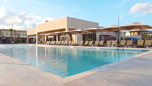 A swimming pool with lounge chairs and umbrellas, surrounded by buildings.