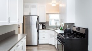 A modern kitchen with white cabinets, a stainless steel refrigerator, a coffee maker, a sink, and a black stove.