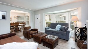 A living room with a grey sofa, brown leather armchairs, and a wooden dining table.