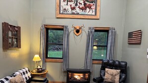 Un salón acogedor con chimenea, cortinas de cuadros y un cojín con motivos de ciervo en el sofá.