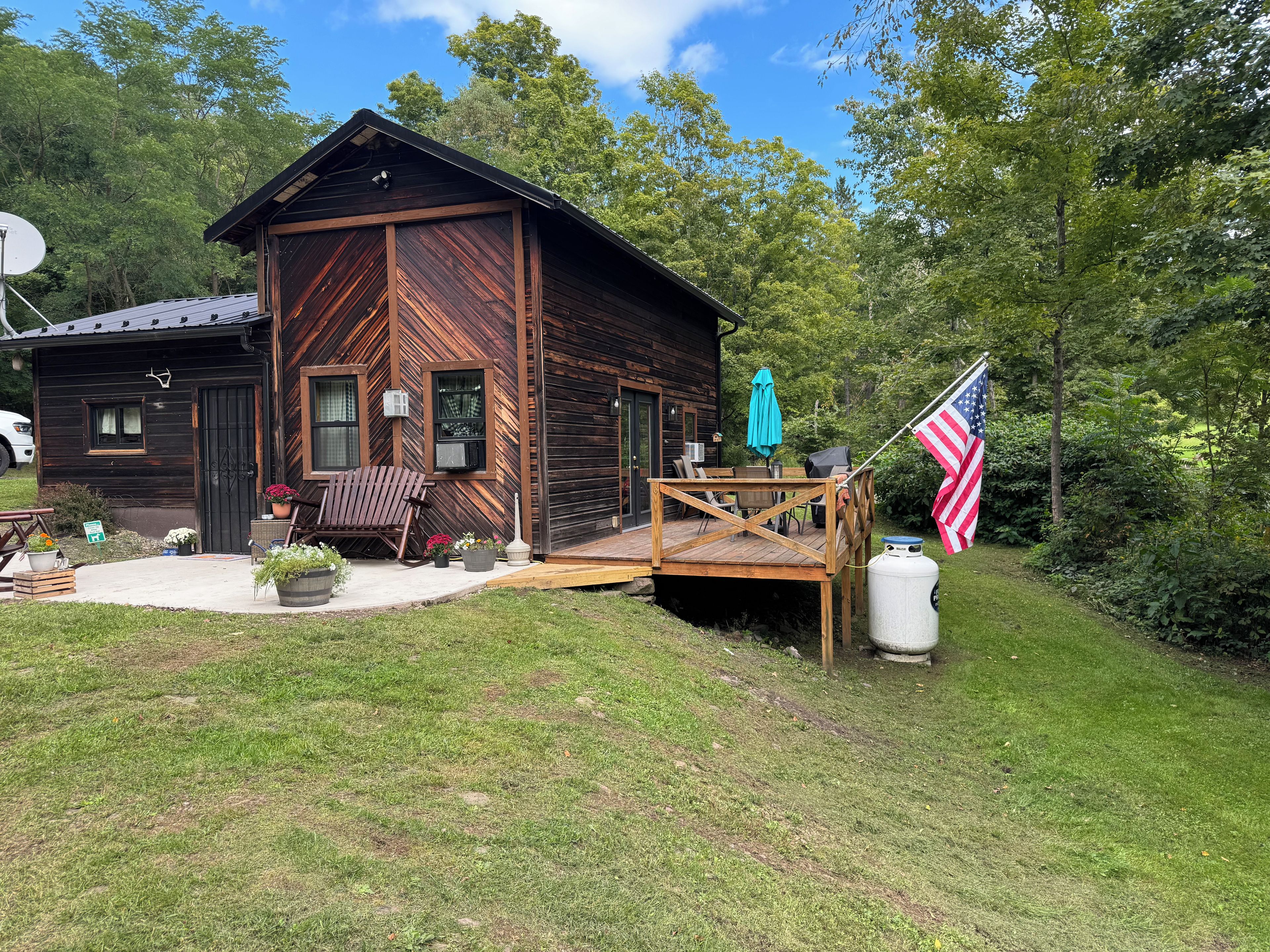A wooden cabin with a porch, outdoor seating, and an American flag.