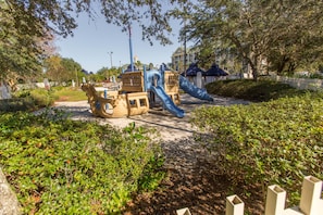 A playground with slides and climbing structures surrounded by greenery.
