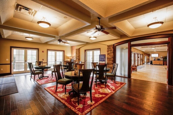 A spacious dining area with a high ceiling, large windows, and a view into the kitchen.