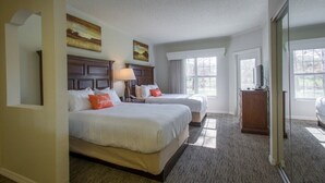A hotel room with two beds, a desk, a television, and large windows.