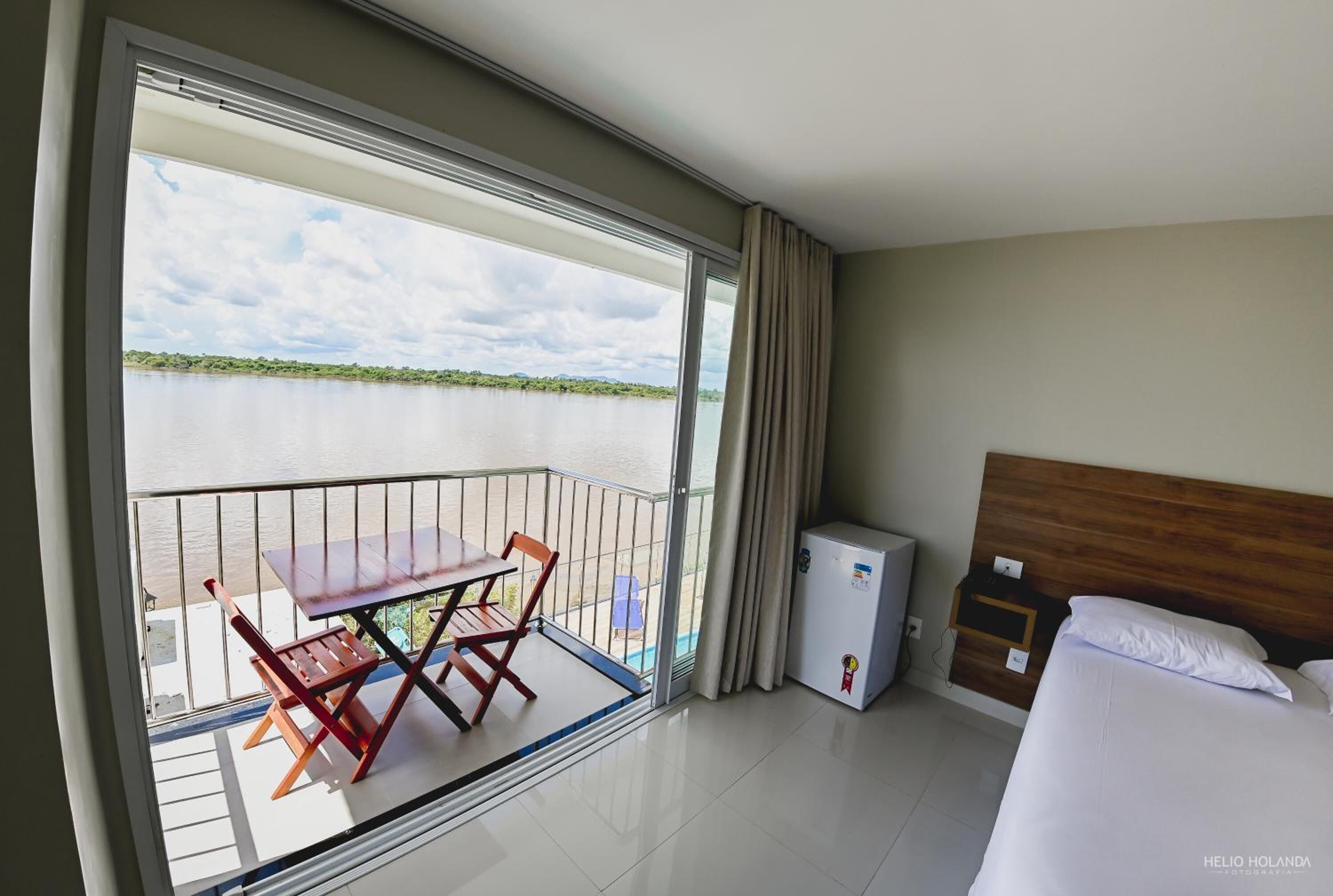 Ein Hotelzimmer mit Balkon, einem Bett, einem kleinen Nachttisch und einem Kühlschrank.