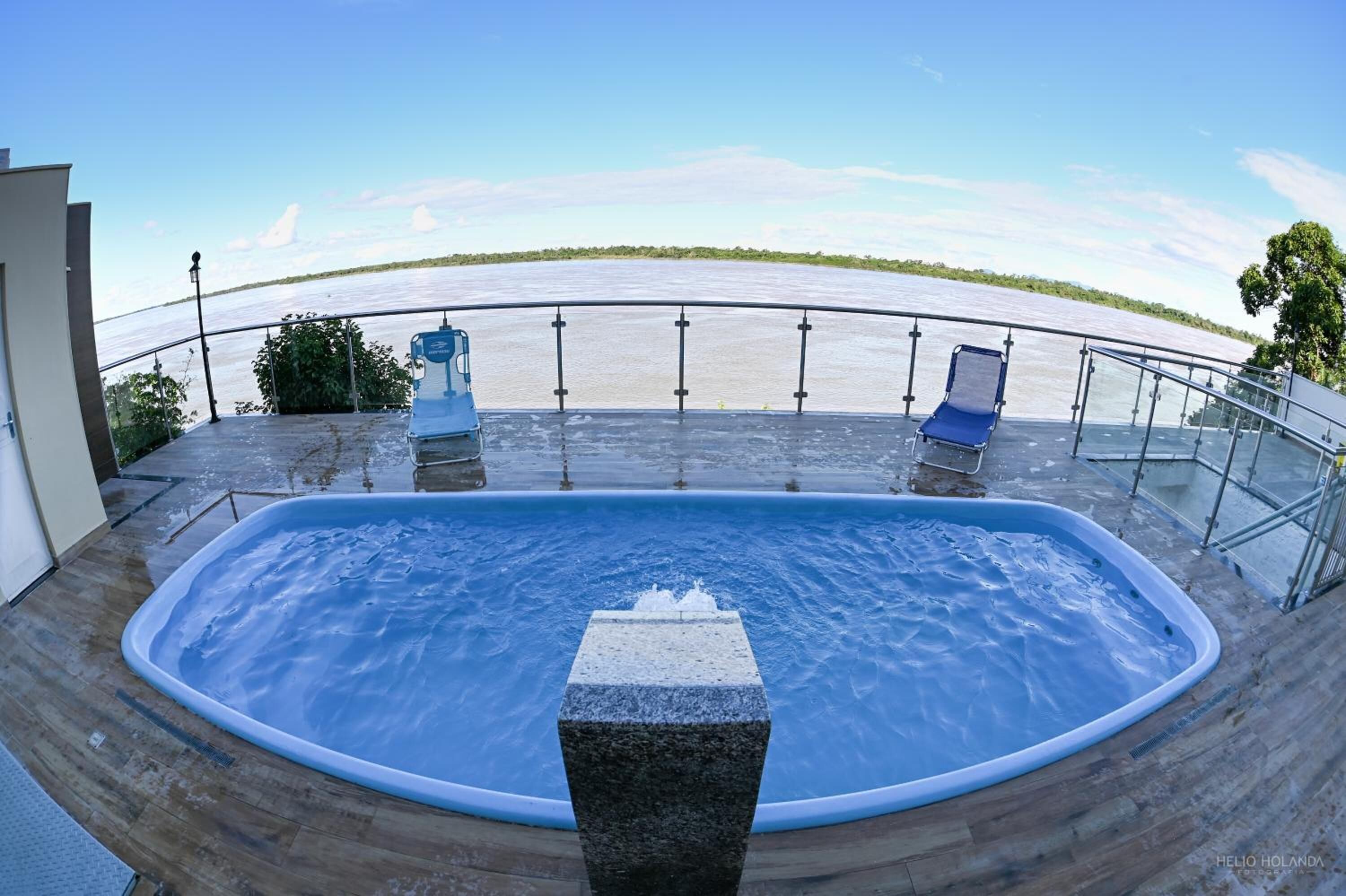 A hot tub with a view of a river, surrounded by a wooden deck and metal railings.