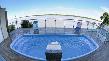 A hot tub with a view of a river, surrounded by a wooden deck and metal railings.