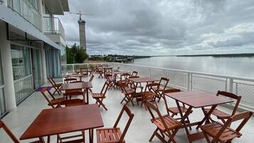 An outdoor terrace with tables and chairs, overlooking a body of water and a distant tower.